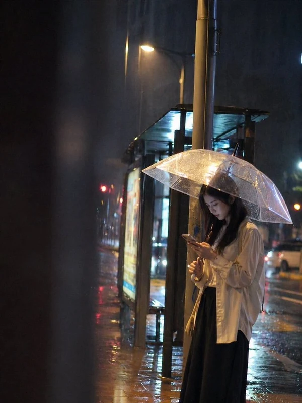 Adult woman holding a clear umbrella at a rainy bus stop